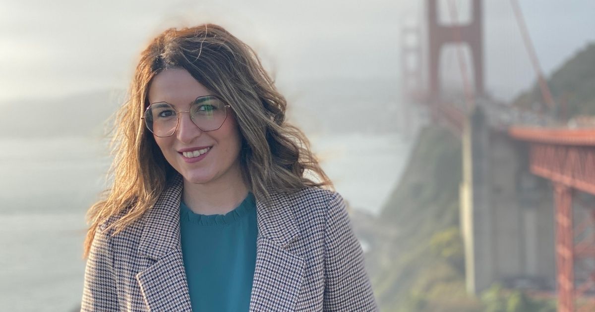 Ines Zuna, '22 MBA/MD, wearing glasses and a patterned blazer smiles at the camera, with the Golden Gate Bridge visible in the background.