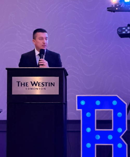 Edward Acuna holds a microphone at a presentation held at the Westin Edmonton; the lighting behind him is purple