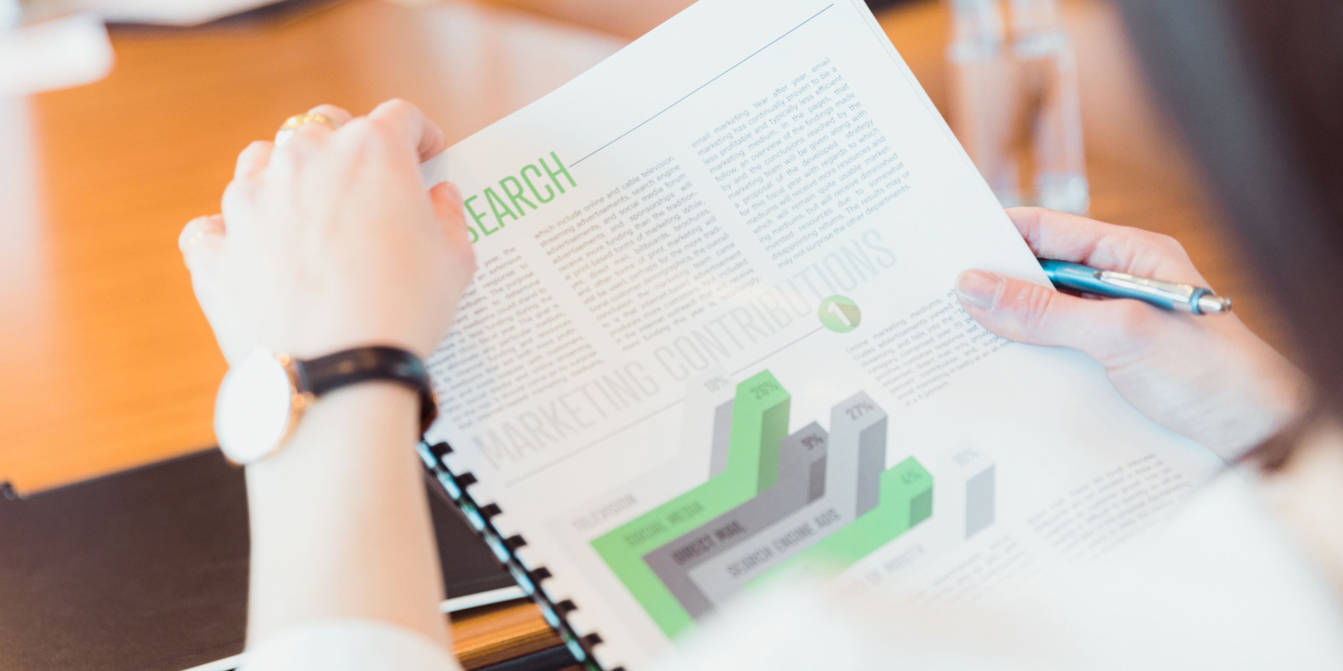 Close-up of a person holding a printed report with charts and text at a conference table.
