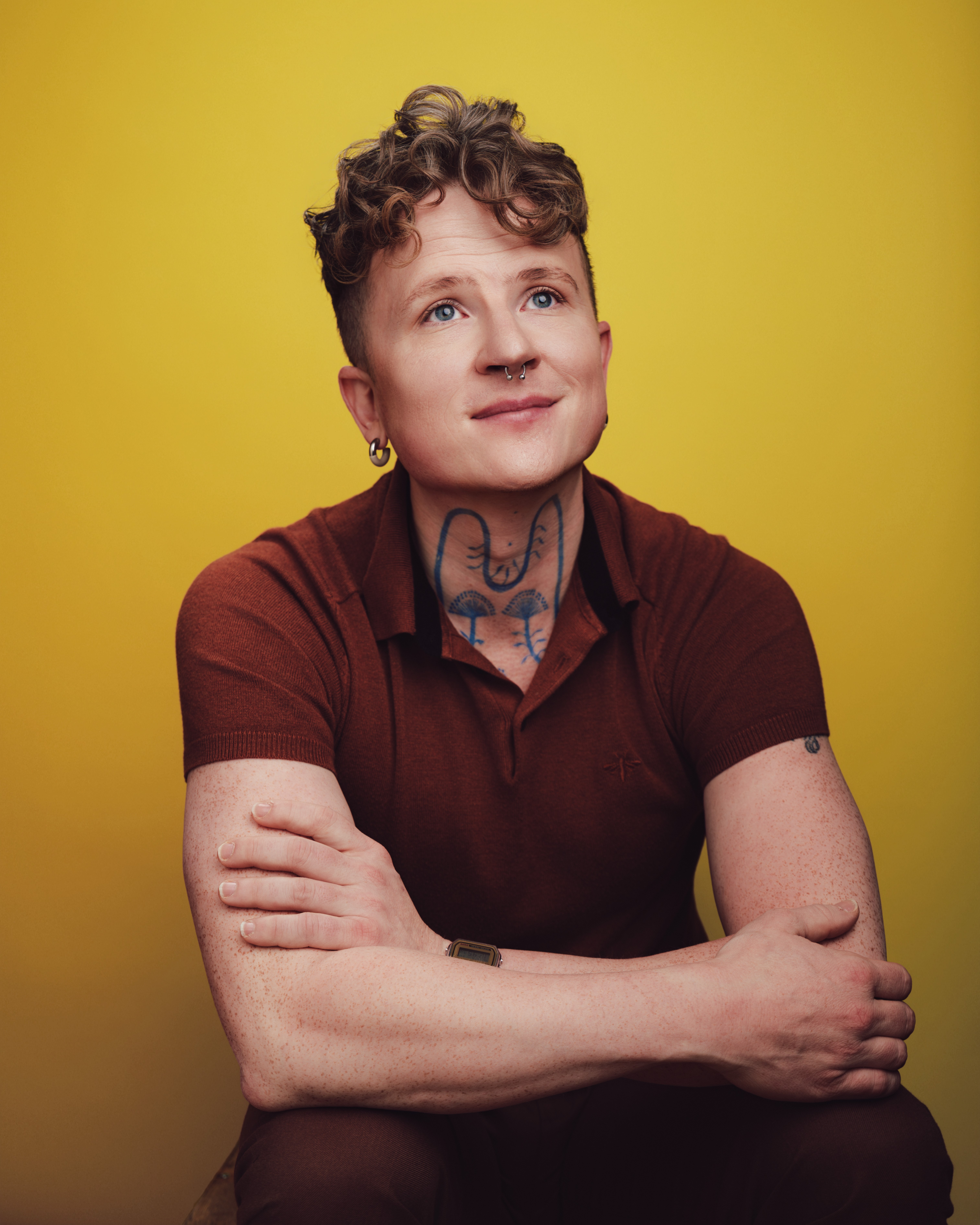 A professional portrait of Tyler in front of a yellow background, arms crossed