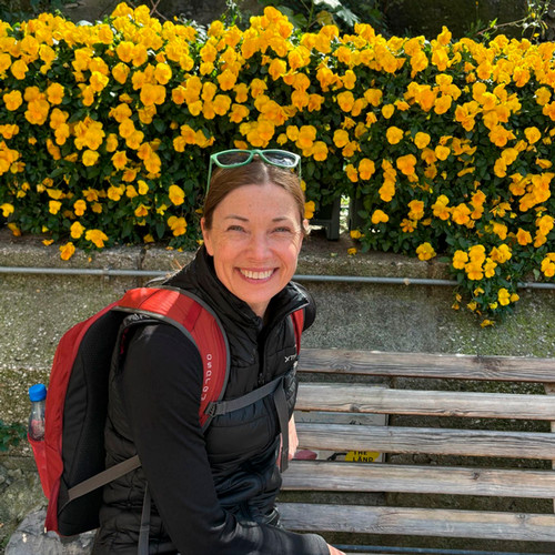 Cosette Lemelin away from her desk, in front of a bright bush of yellow flowers.