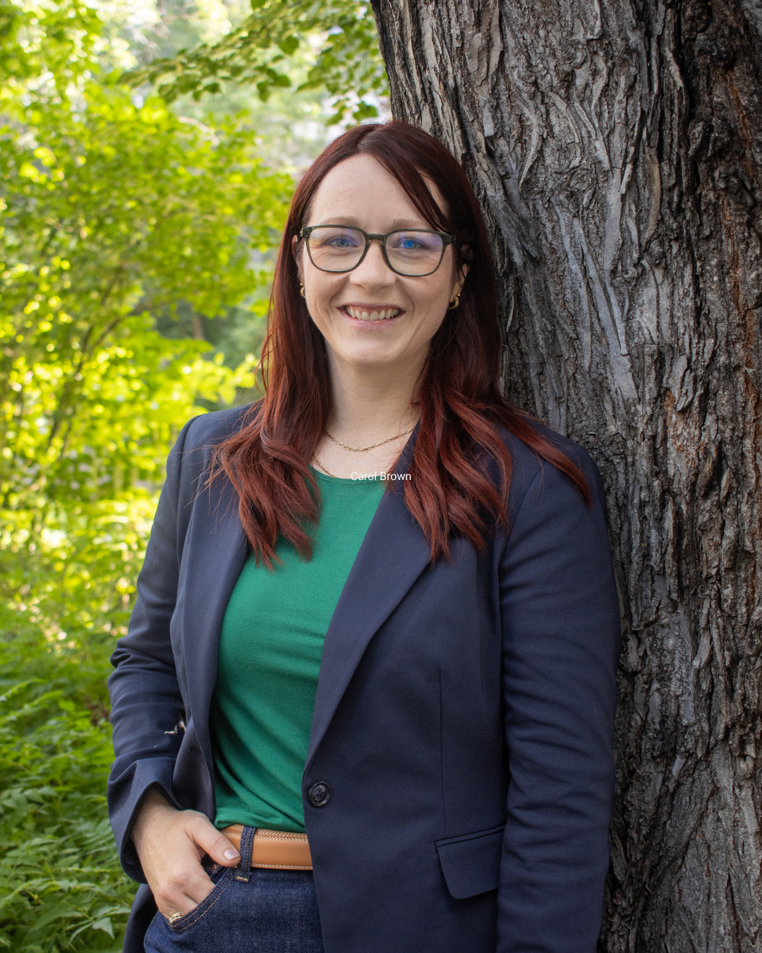 Carol Brown in glasses and blazer in front of a tree with green leaves