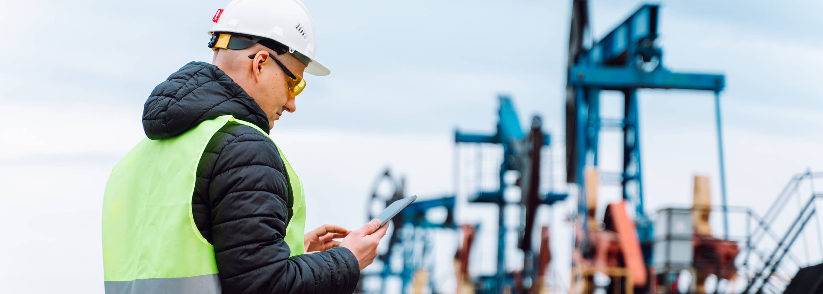Drill worker calculating data on tablet, oil refinery tasks near pump jack, processing facility