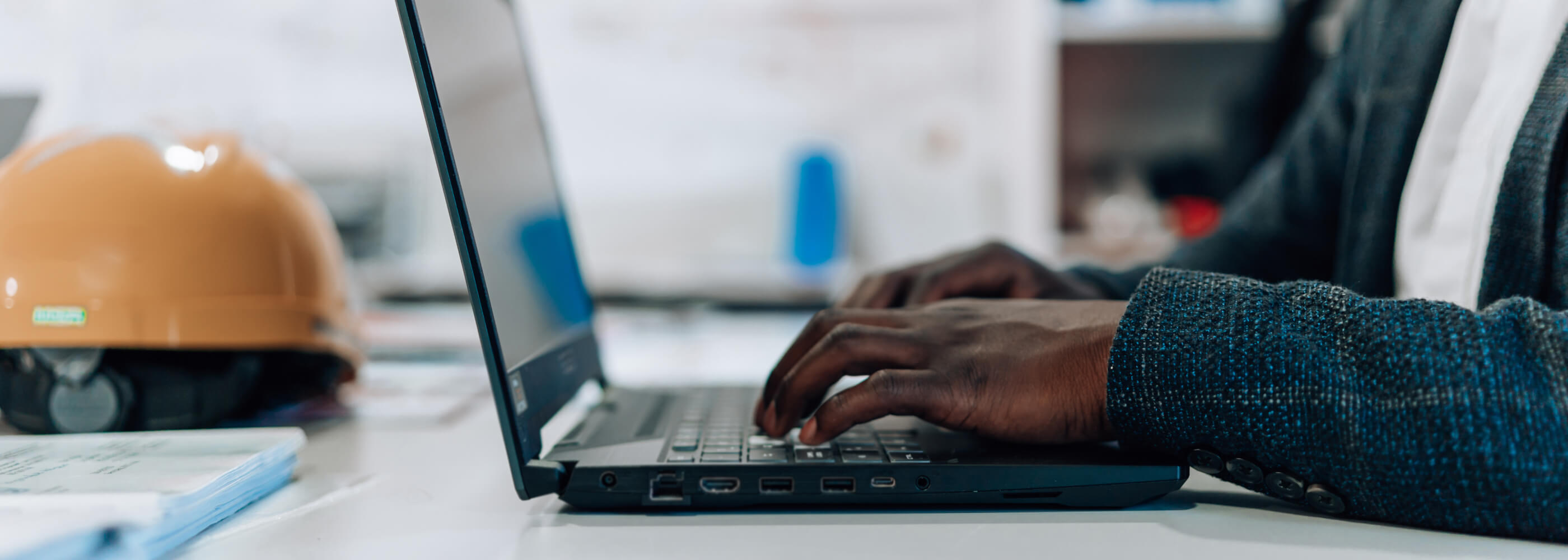 A close-up of a young engineer typing on his laptop, while sitting at his desk.