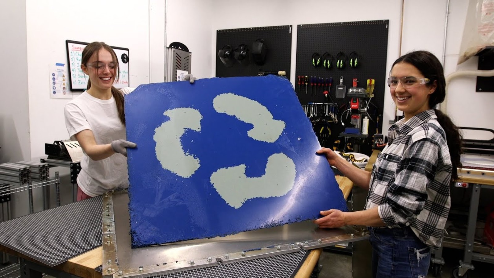 Two students holding up a plastic sheet with the recycle symbol
