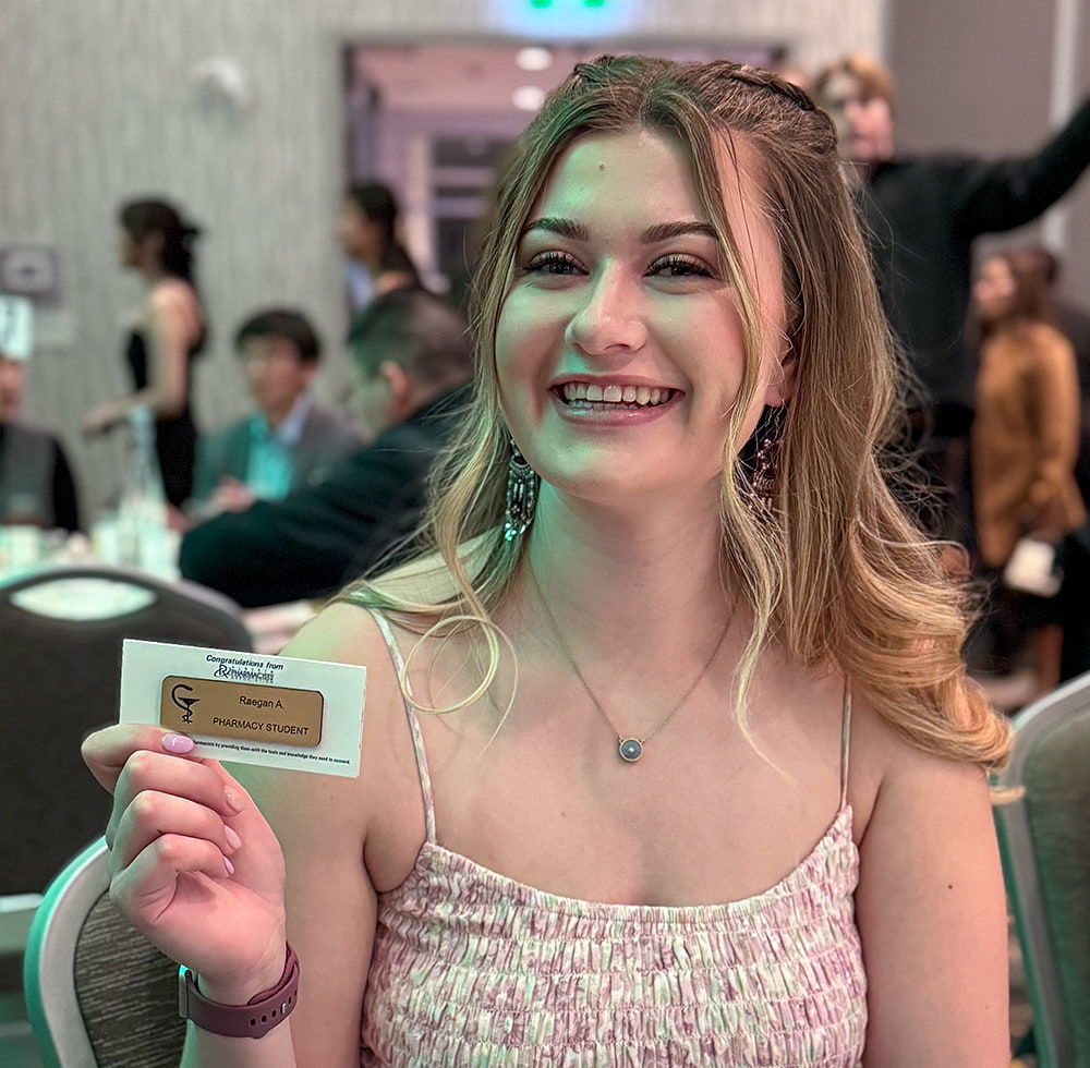 Pharmacy student Raegan Abrey hold up her pharmacy student name tag at the white coat ceremony for the Faculty of Pharmacy and Pharmaceutical Sciences.