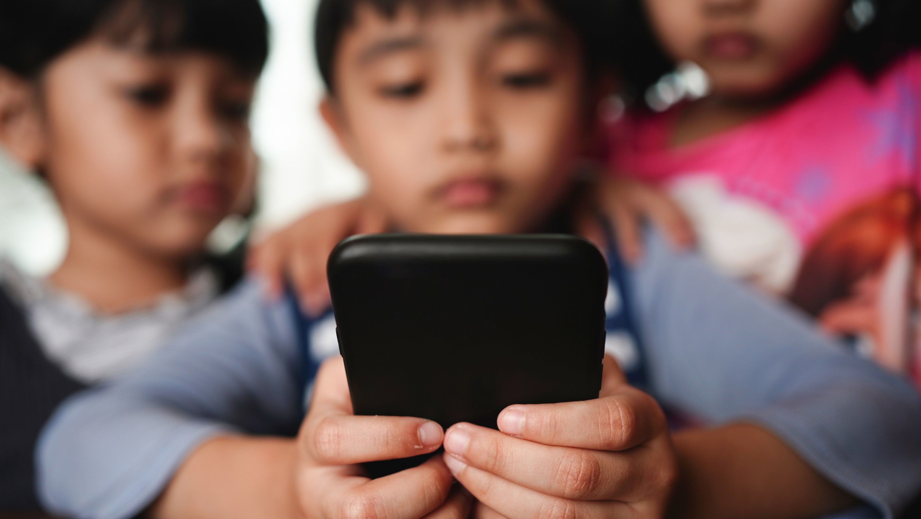 A group of three children look at a phone screen. (Photo: Getty Images)