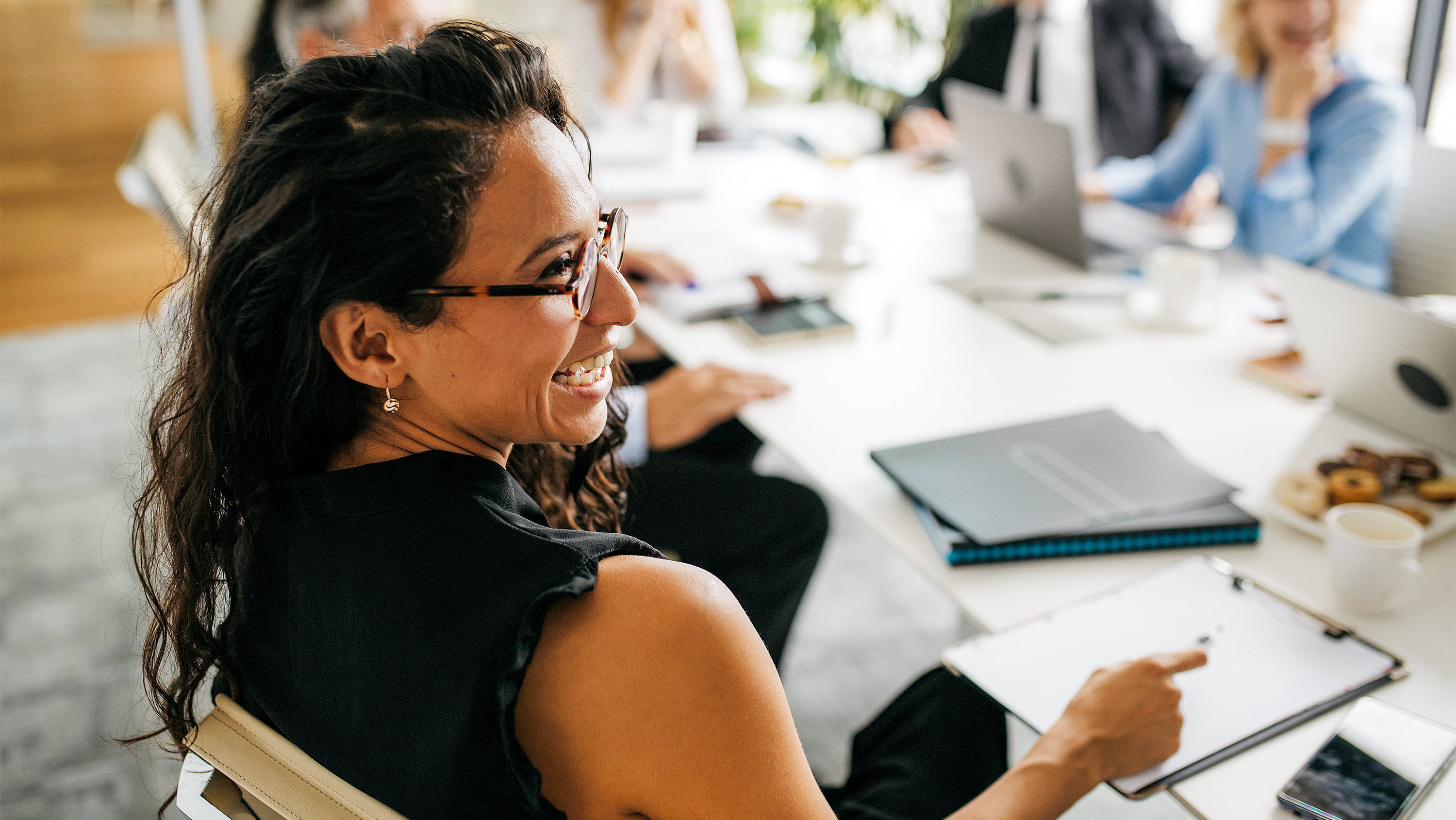 A smiling woman sits at a conference table with her colleagues. (Photo: Getty Images)