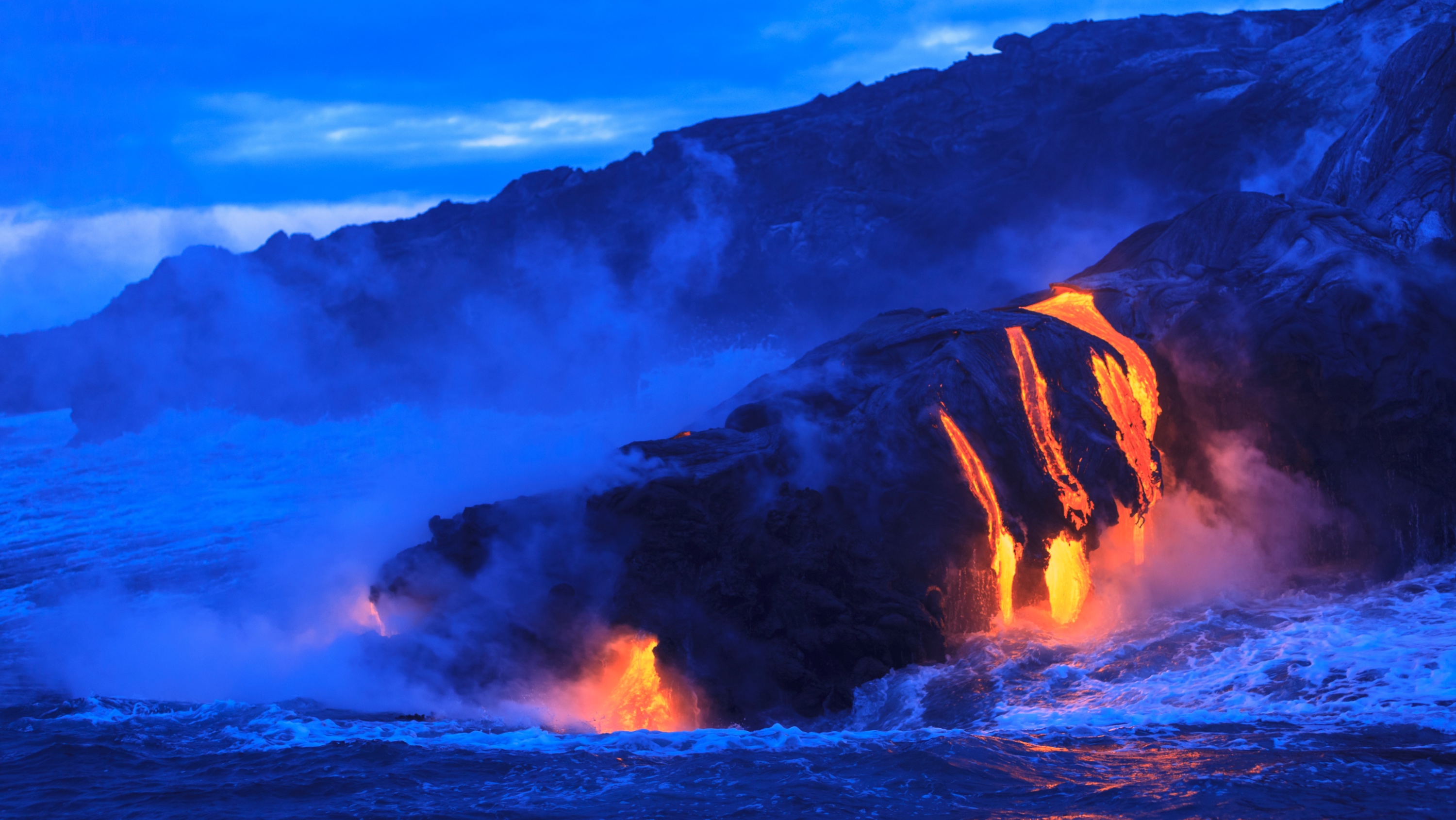 Lava flows down cliffs near an ocean. (Photo: Getty Images)