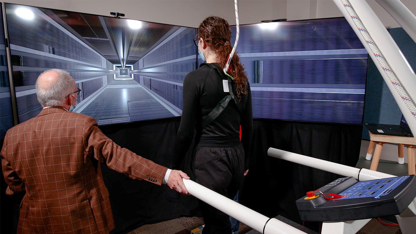 A woman walks on a treadmill towards a screen displaying an elevator shaft. (Photo: Geoff McMaster)