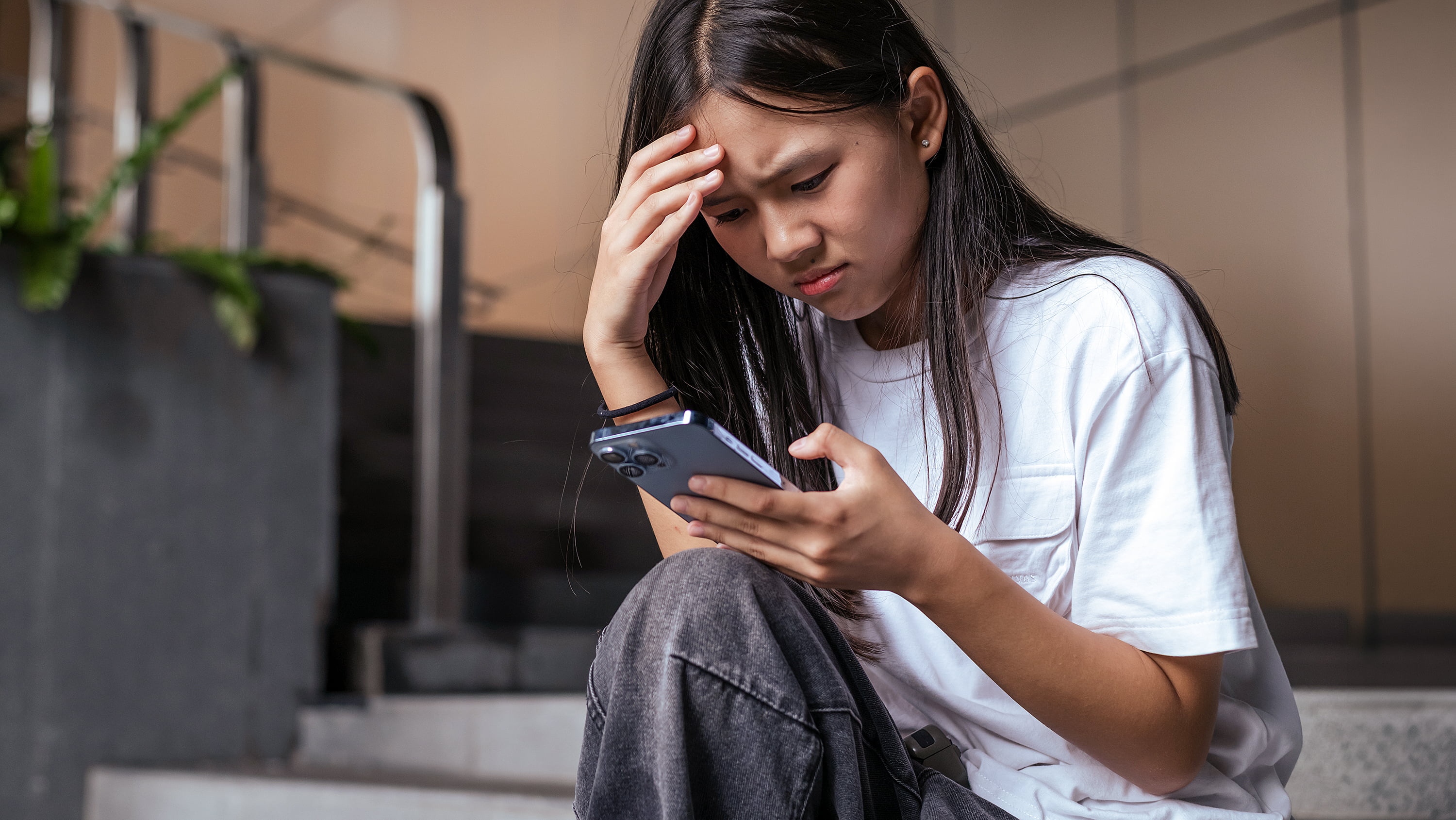A teenager with a distressed look on her face clutches her head and gazes at her phone. (Photo: Getty Images)