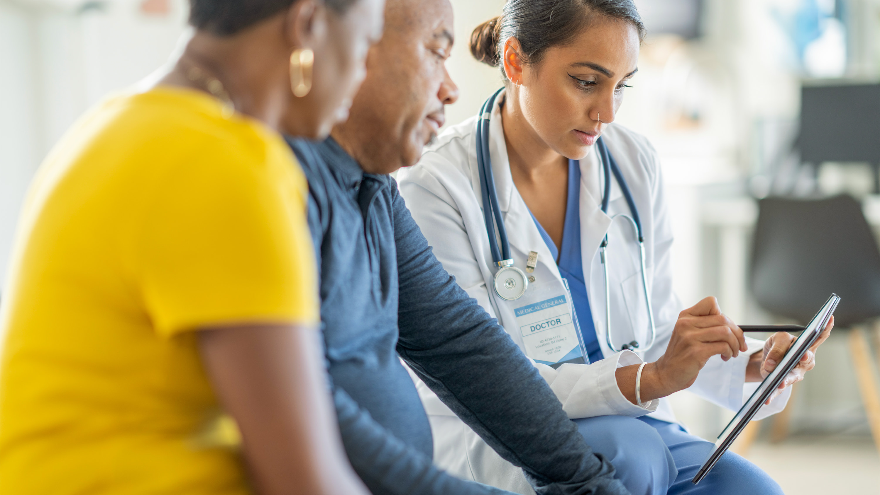 A doctor uses a digital tablet to review medical information with a couple sitting beside her in a clinical setting. (Photo: Getty Images)