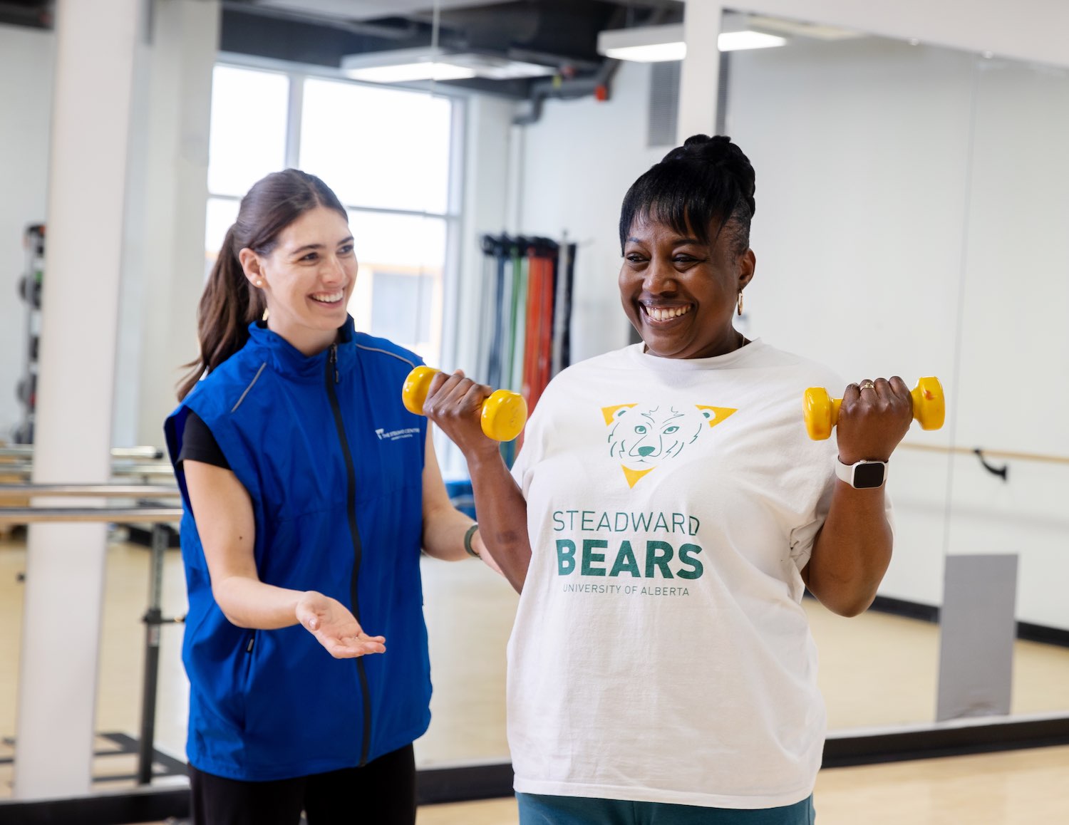 Woman wearing a Steadward Bears shirt exercising with freeweights under supervision of a Steadward researcher
