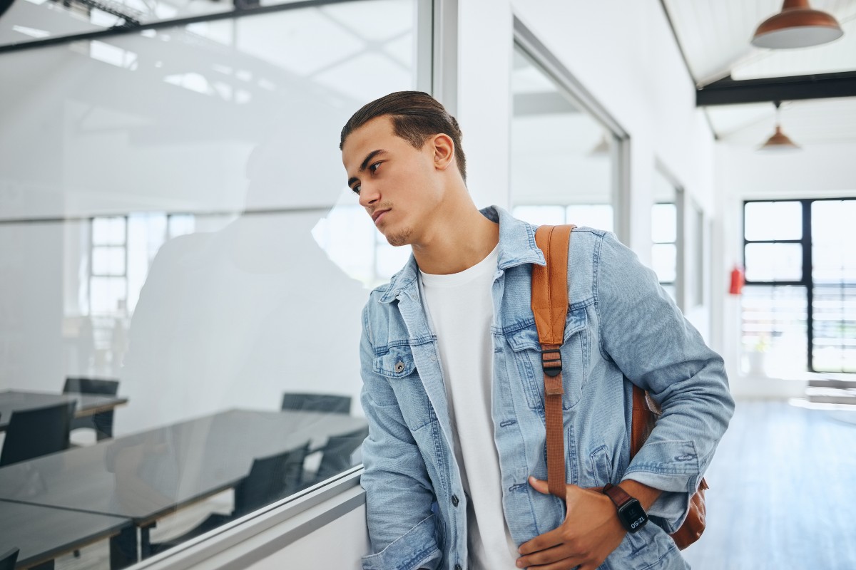 A student leans against a window, looking into a classroom. 