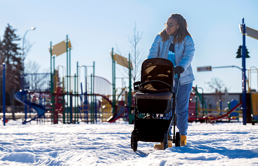 Winter photo of Josephine Godwyll pushing a stroller at a city park, blue sky in the background