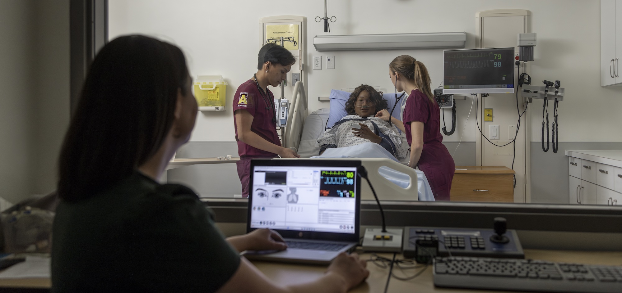 Nursing students working with a dummy in a simulation room with an instructor manipulating the scenario