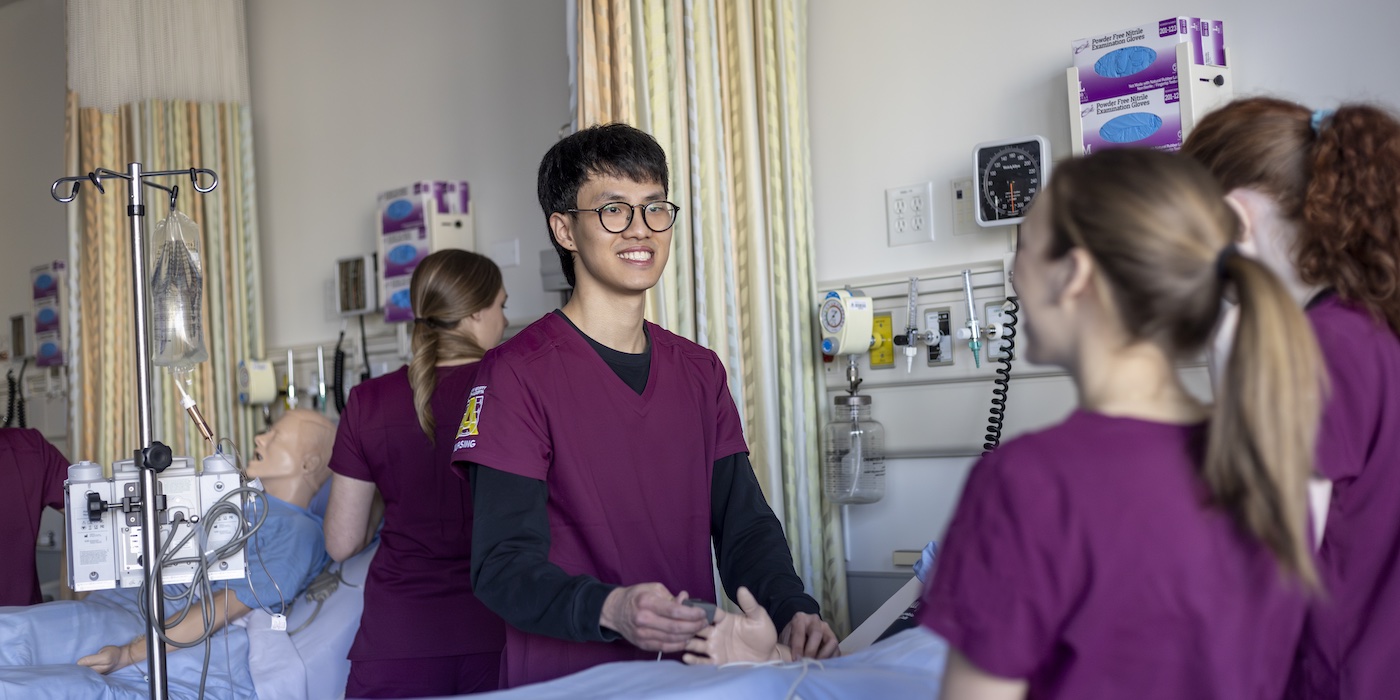 Three nursing students working with a dummy patient in a hospital bed setting