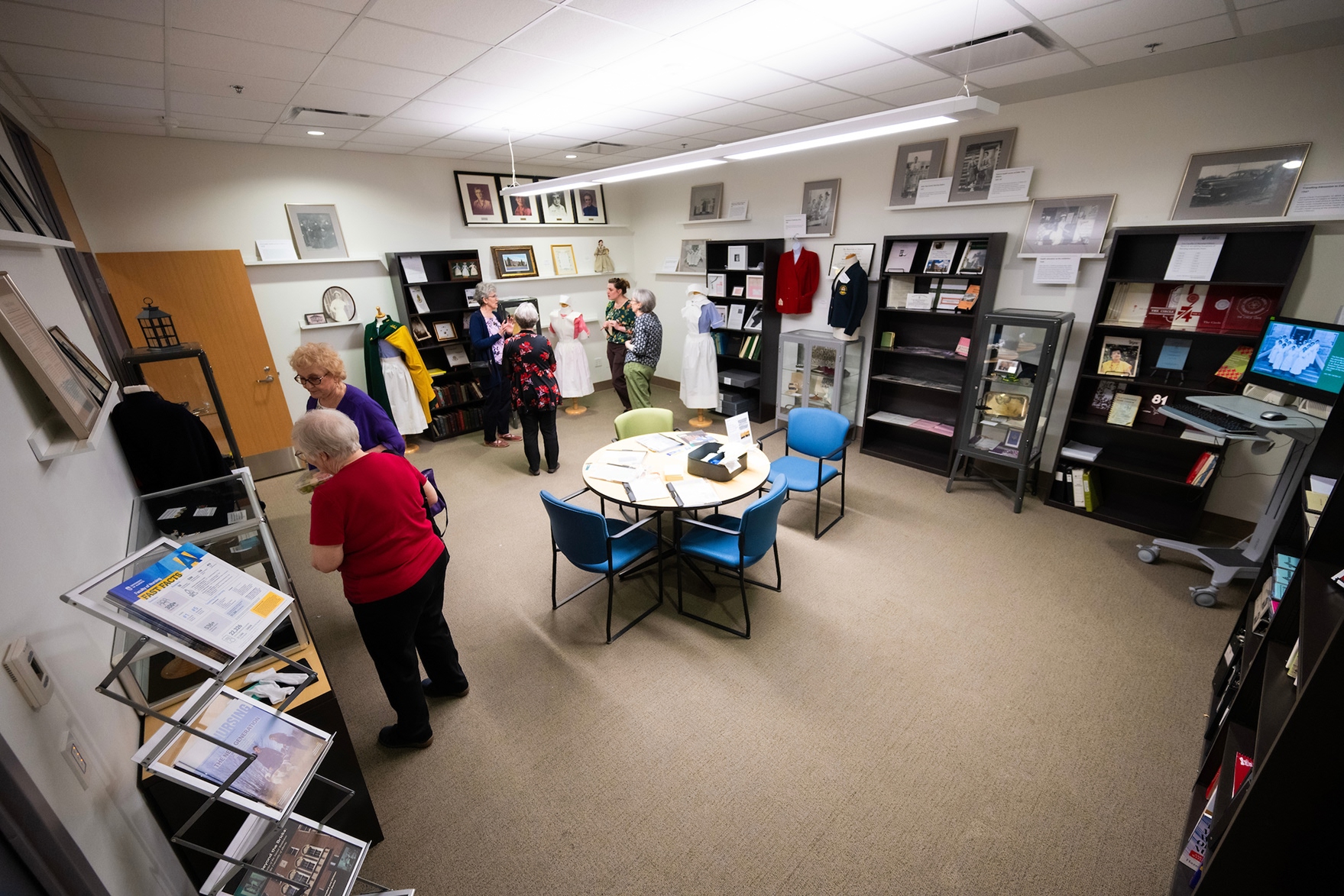 Wide view of a nursing history museum room with display shelves, mannequins, historical artifacts, and visitors exploring the exhibit space.