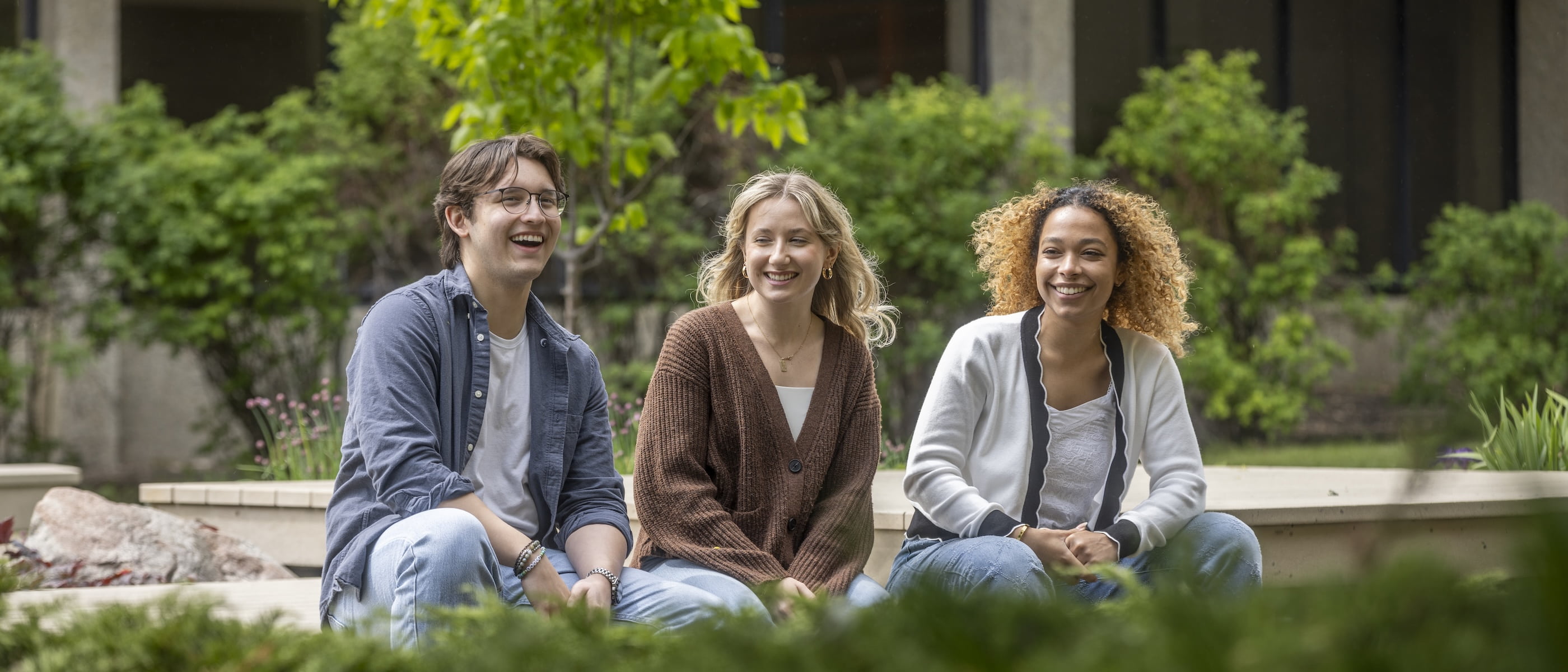 three smiling students sitting outside