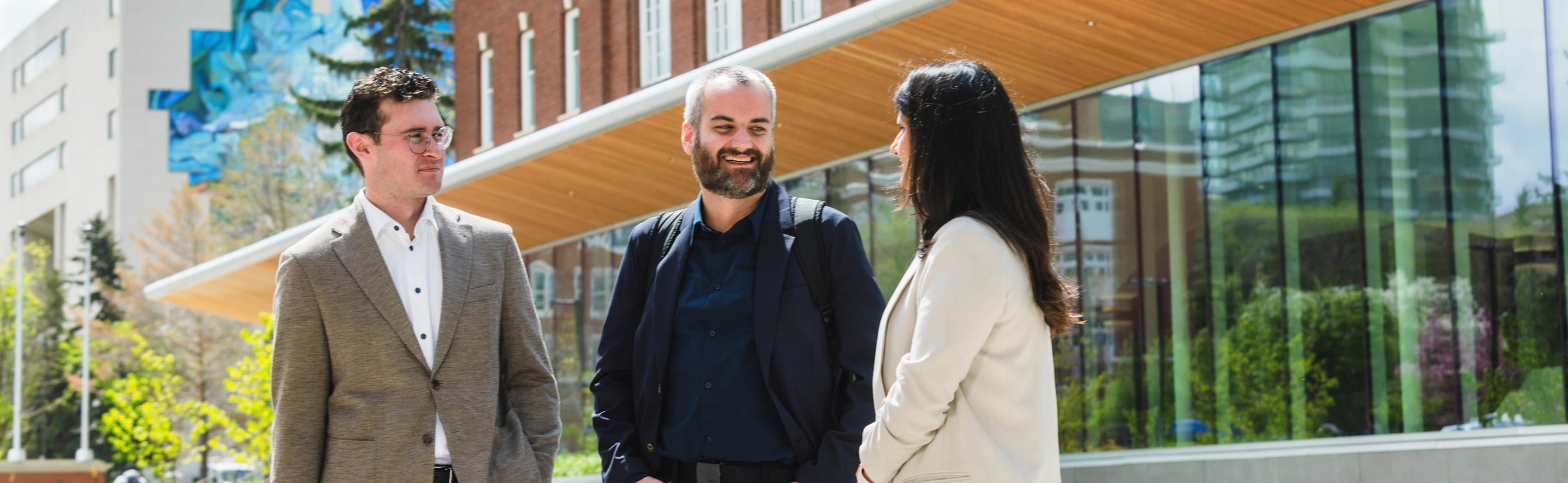 Three professionals talking outside a modern university building.