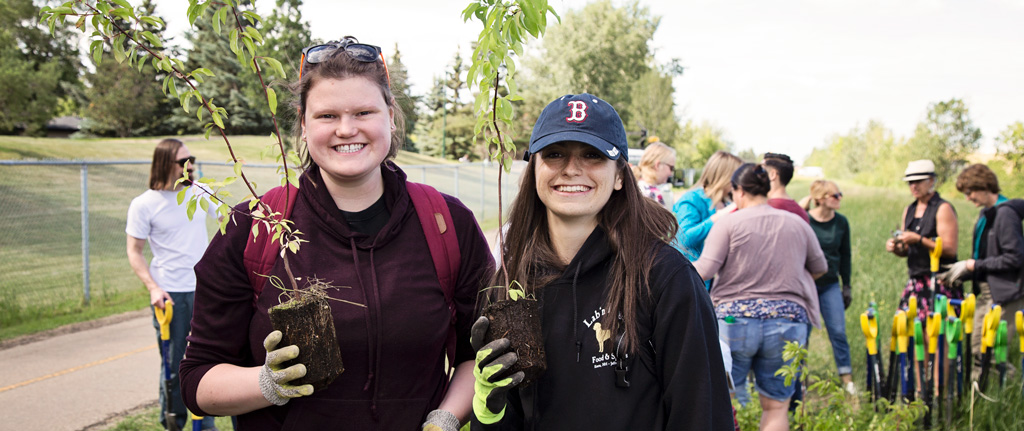 Two alumni women holding plants they are going to plant in the ground.