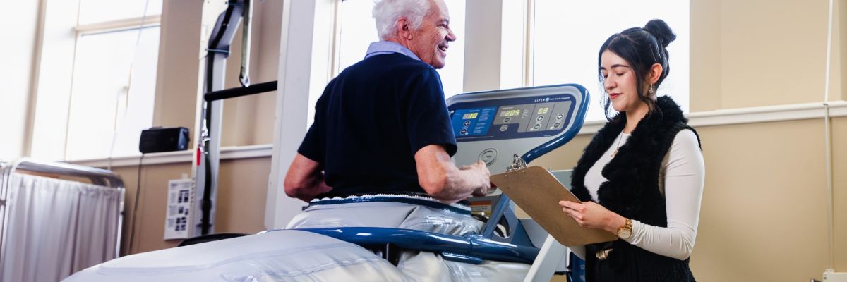 Person running on treadmill with clinician standing beside them