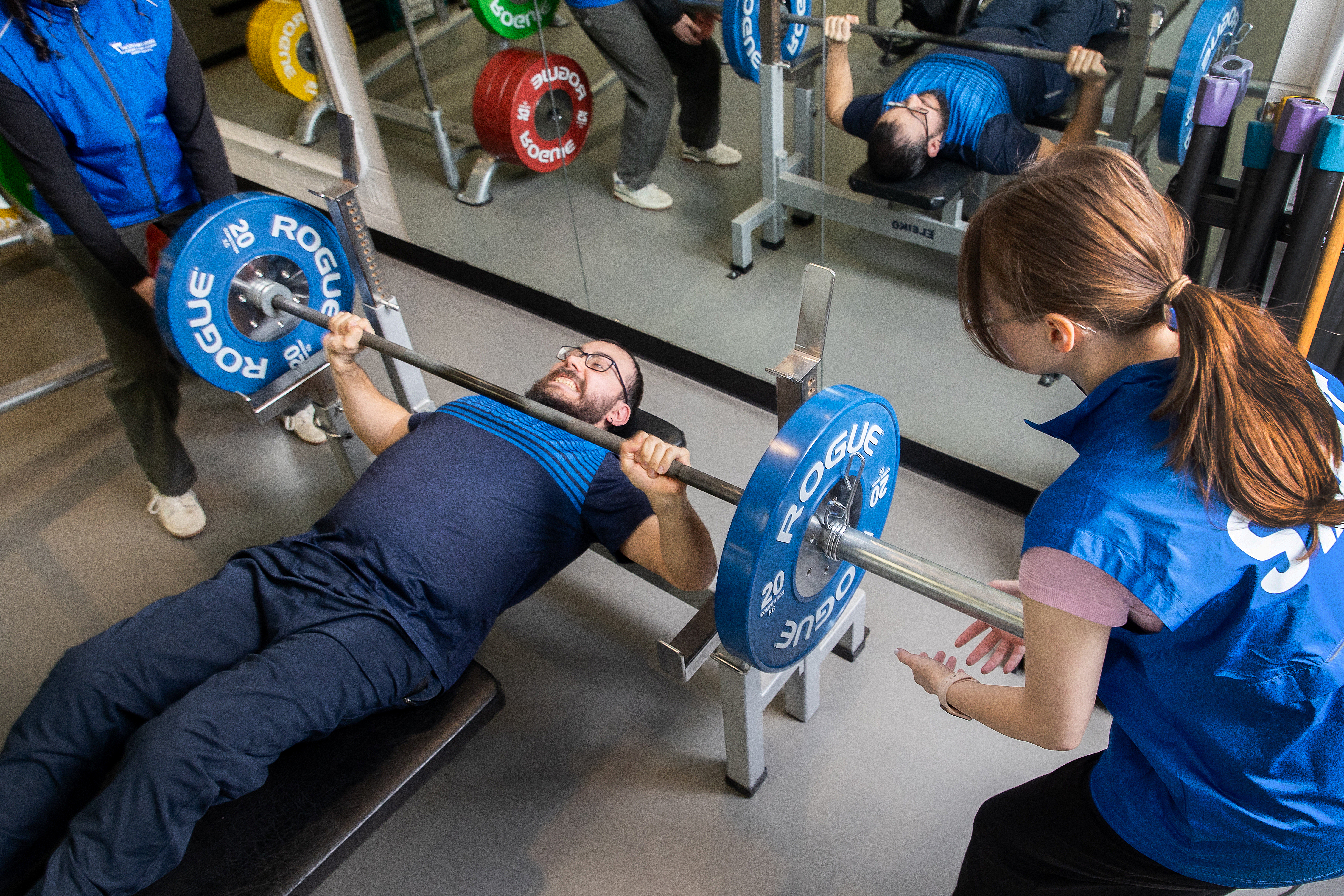 Image of TSC member powerlifting with two APA Consultants in blue on either side.