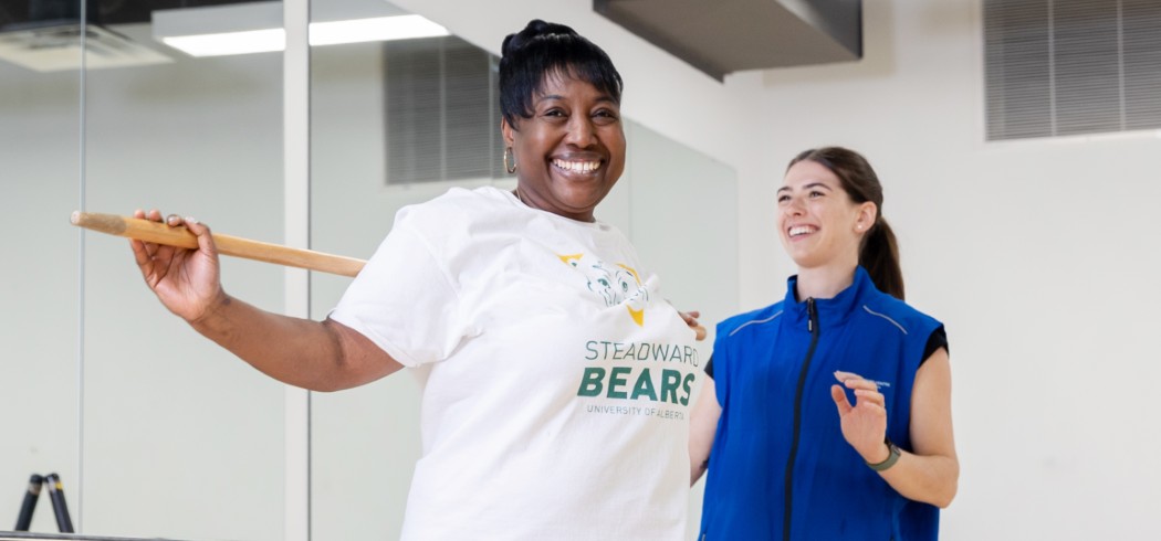 Woman with a wooden bar across her shoulders with a fitness instructor