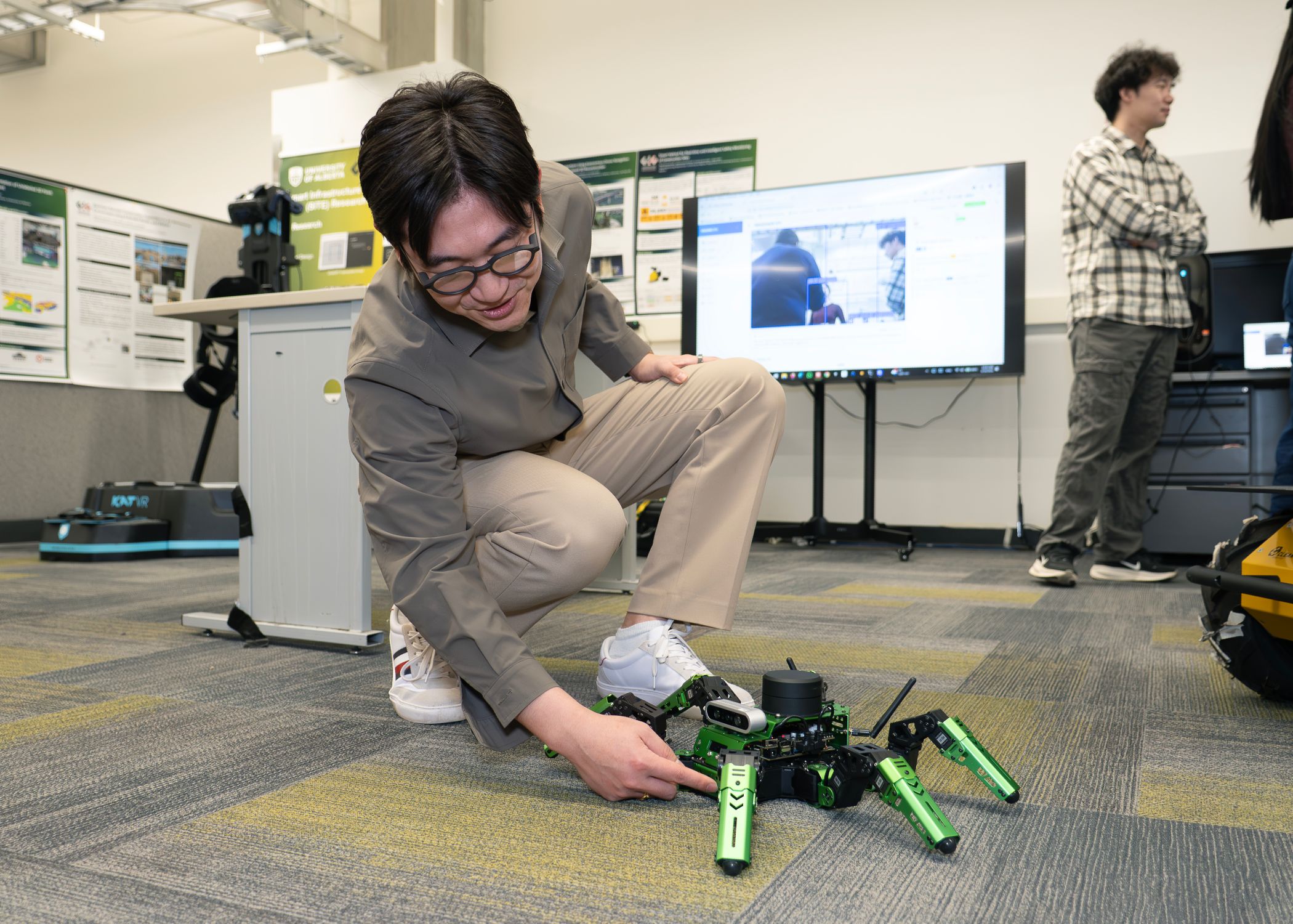 Zhong Wang, a graduate research assistant fellow, interacts with a hexapod robot on the ground during a robotics experiment.