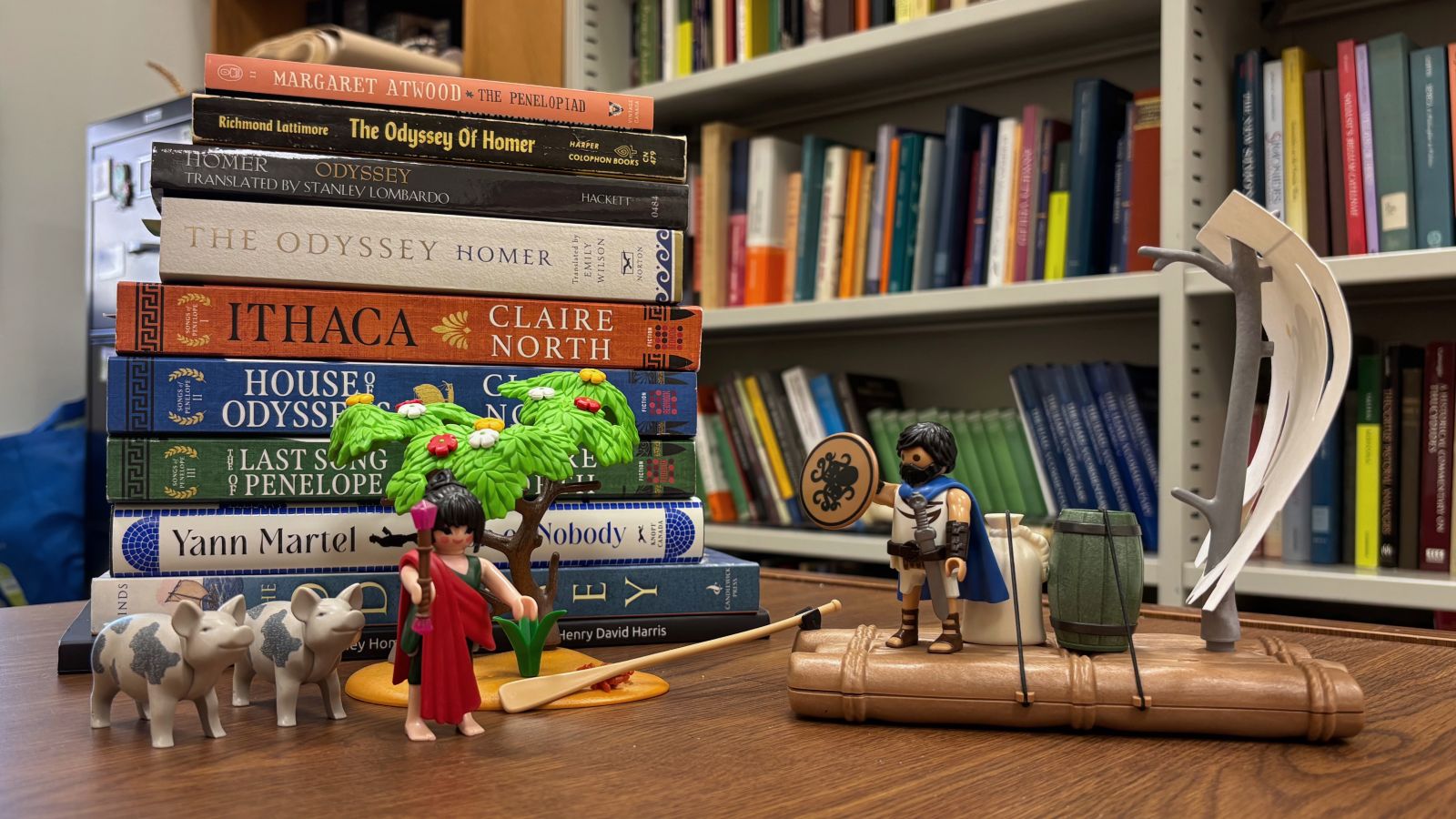 Multiple editions of the book The Odyssey arranged together with Greek warrior LEGO figures placed next to them.