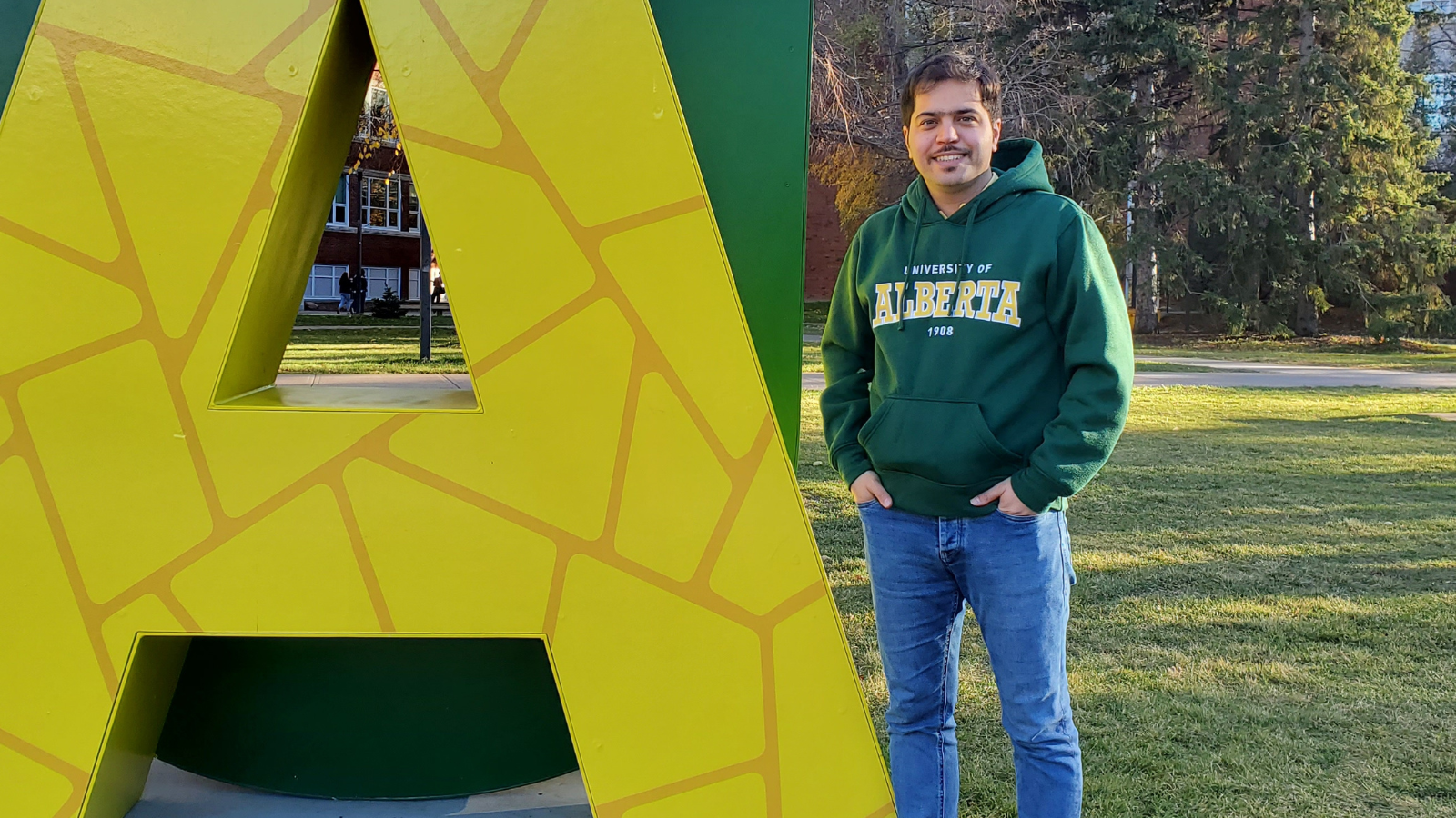 Portrait photo of student in beside UofA 'logo' on the Quad.