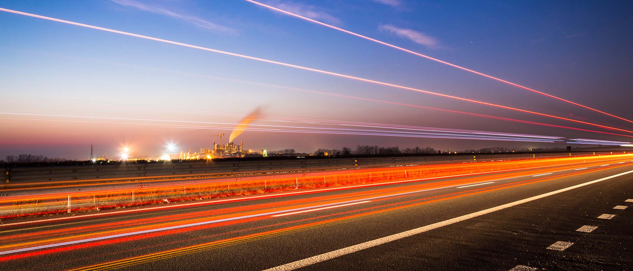Long exposure of traffic on highway next to industrial processing facility.