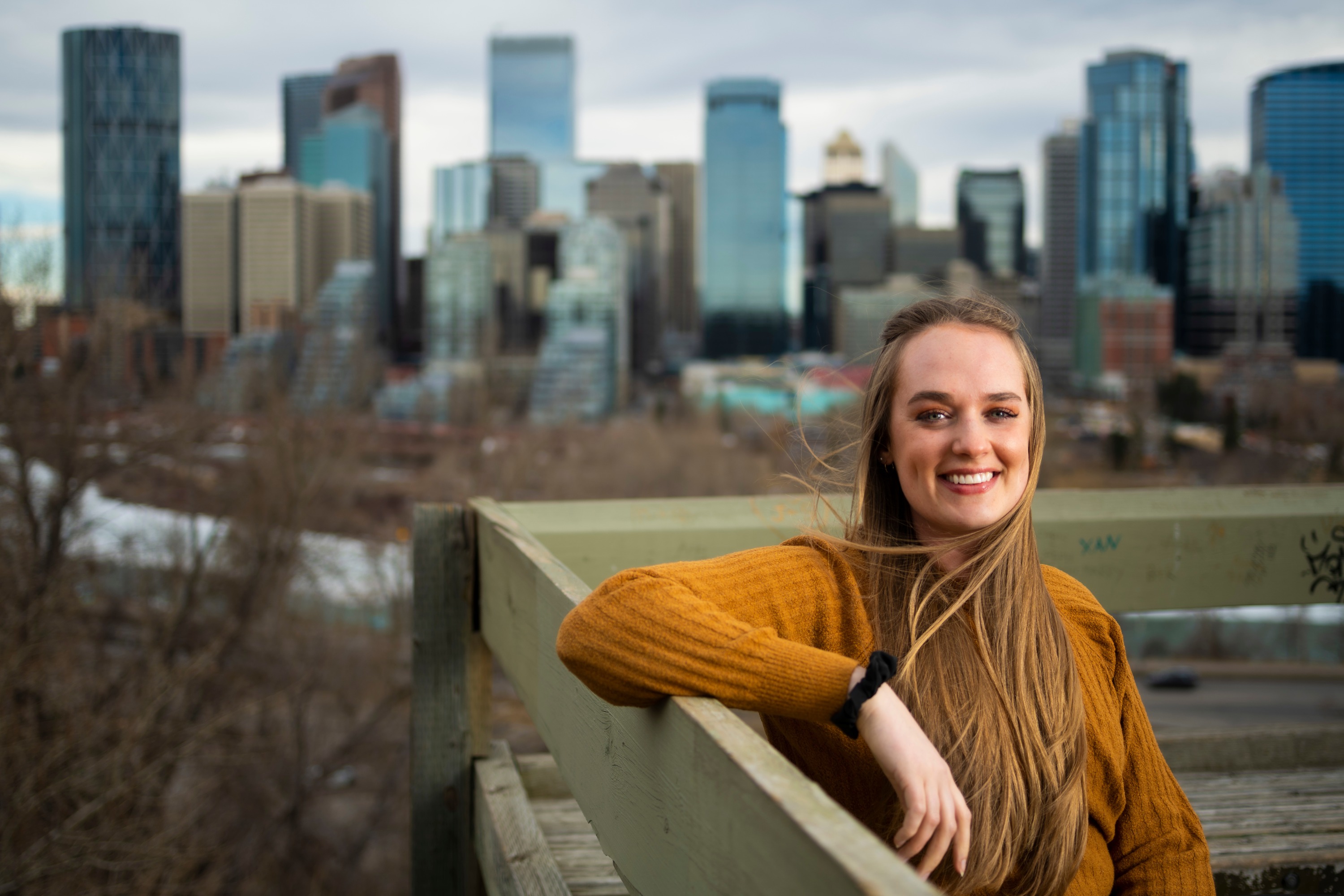 Pharmacy student Olivia Stephen sits on a park bench with the Calgary skyline in the background. (Photo: John Ulan)