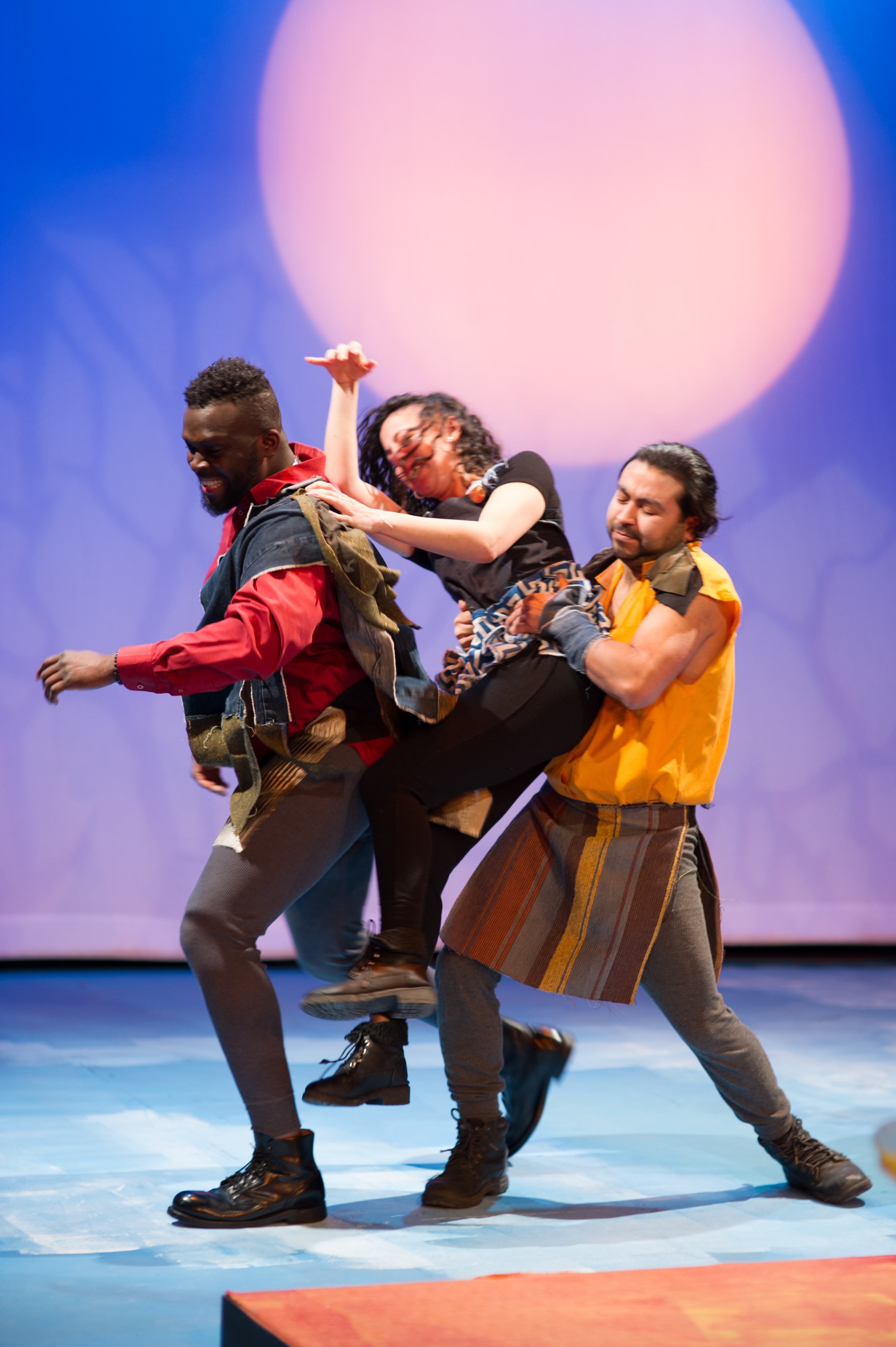 Two students acting on stage carrying another actor.