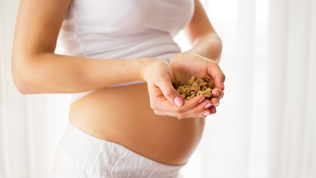 A photo of a woman holding a handful of walnuts over a partially bare pregnant belly.