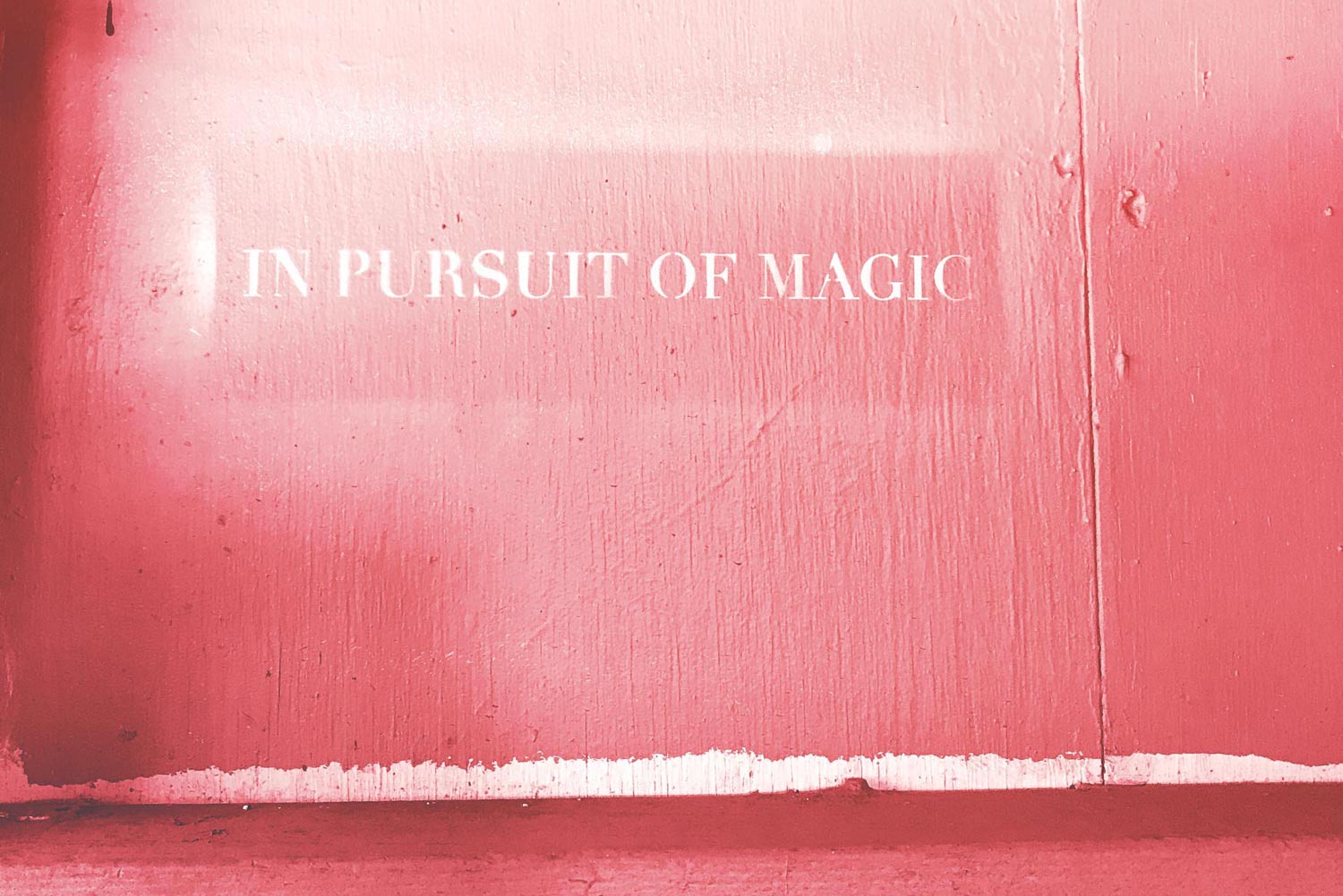 White graffiti of "In pursuit of magic" stenciled onto a red wood wall