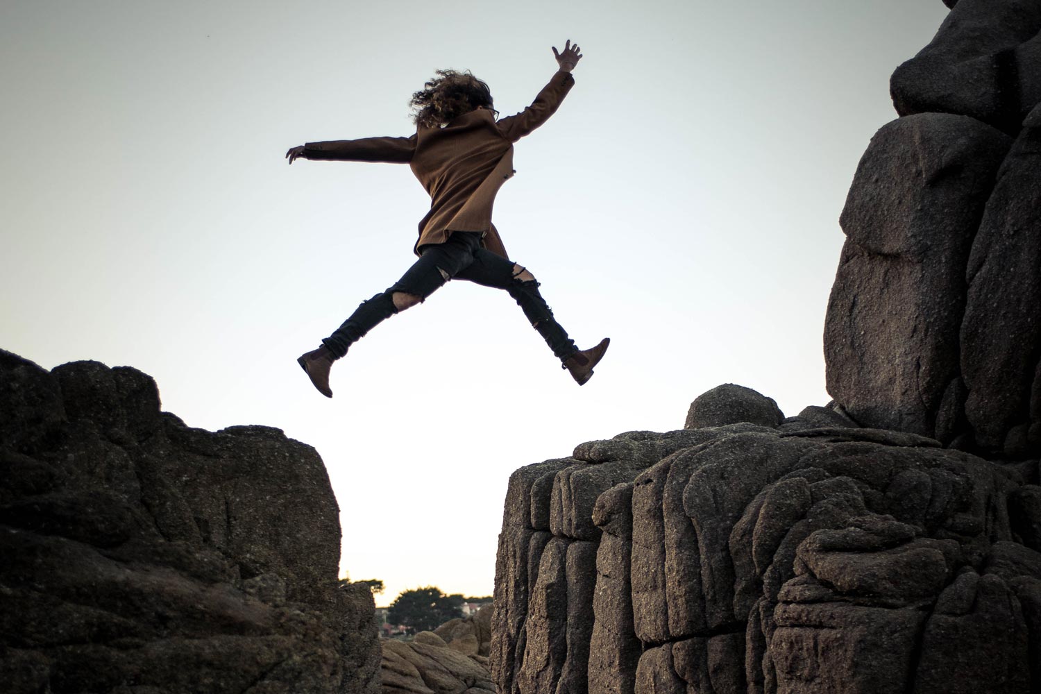 Silhouette of person jumping between two rock ledges
