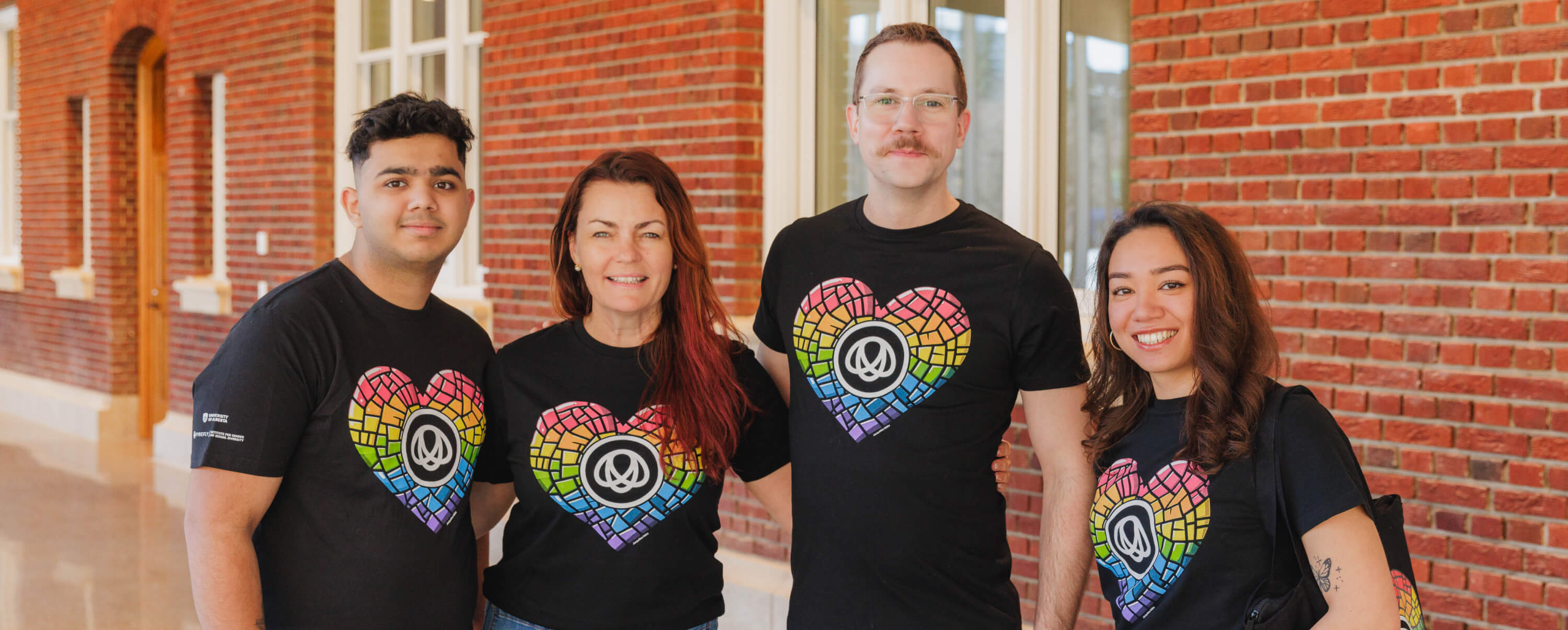 Four people wear UA Pride merch on campus