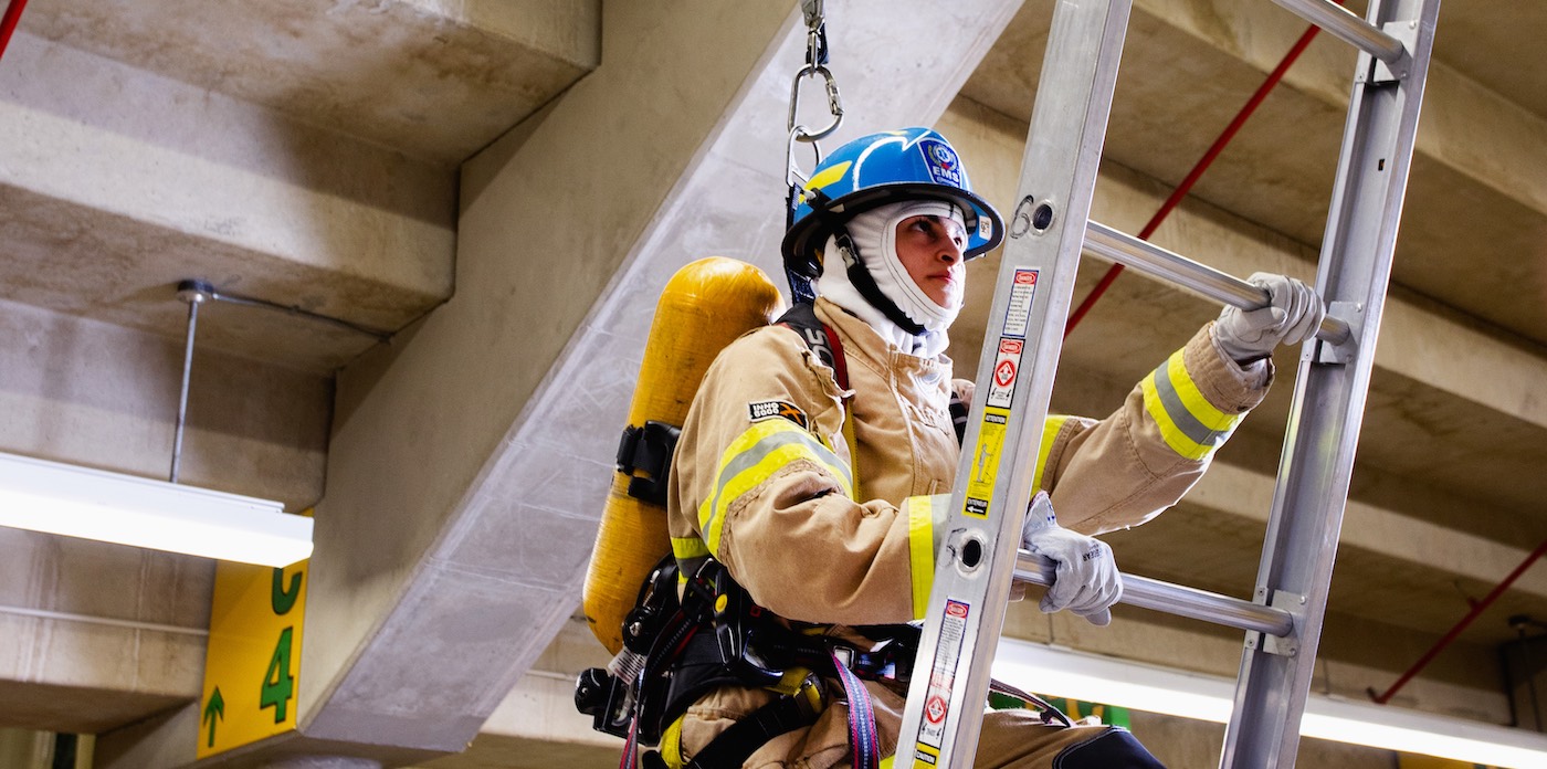 Applicant climbing a ladder wearing full firefighter gear
