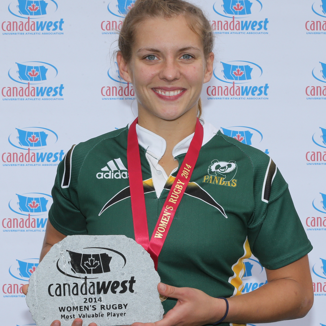 blonde female wearing University of Alberta rugby jersey, wearing a medal and holding an award smiles into camera
