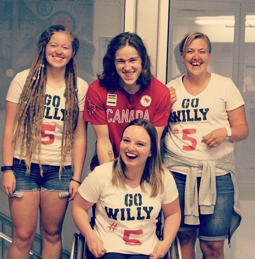 family of four in Team Canada paralympic gear. Three females in white shirts, one of which is in a wheelchair, and one male in a red shirt all smile into the camera