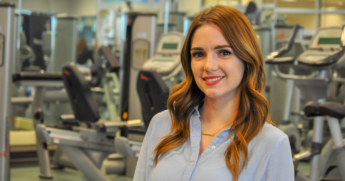 woman with long red hair in light blue shirt poses for camera in fitness centre
