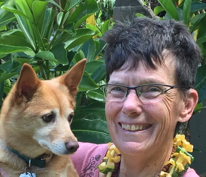 woman in short brunette hair wearing a pink shirt and a yellow Hawaiian lei, holding a golden-coloured dog