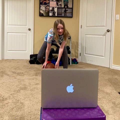 female youth practices basketball skills while watching tutorial on laptop in basement