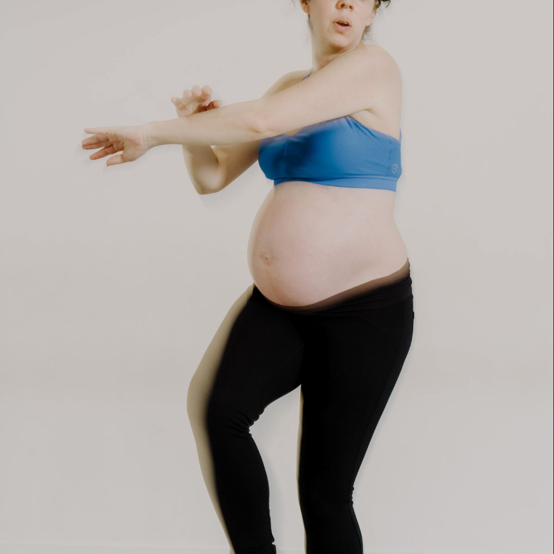 Pregnant Caucasian woman holding standing yoga pose wearing black yoga pants and a blue sports bra