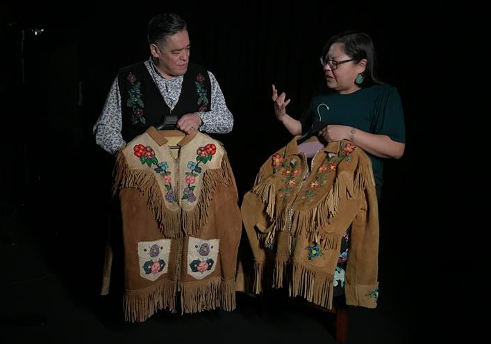 Two people sitting holding beaded jackets