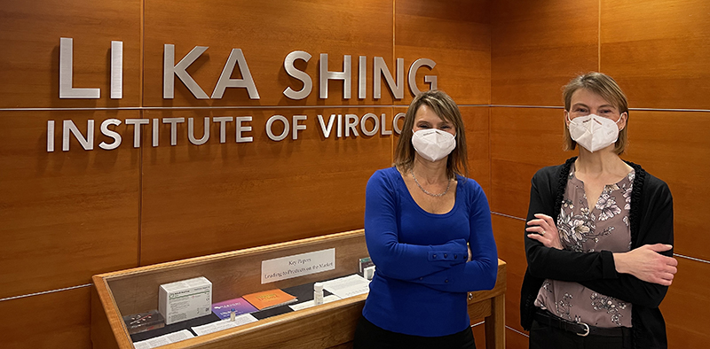 Carrie and Melissa wearing masks and standing in the lobby of the Li Ka Shing Institute of Virology