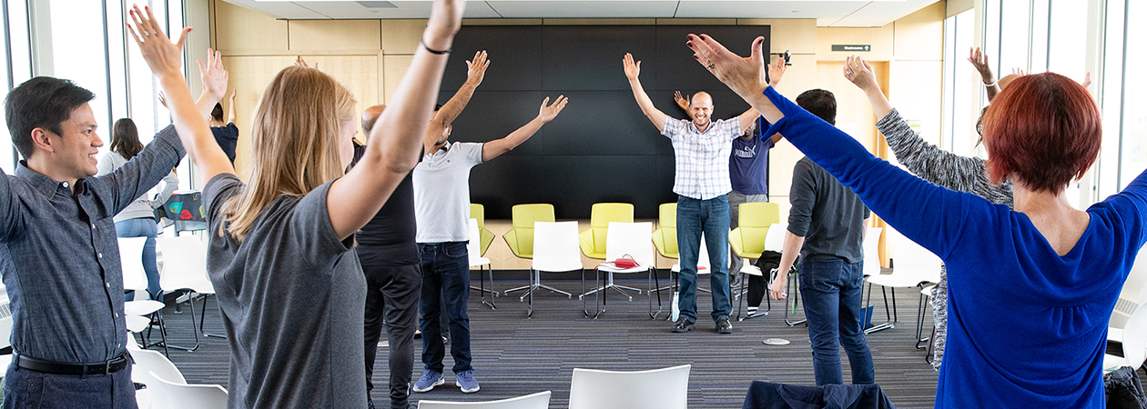 Workshop participants hold their arms in the air in a power pose following the facilitator