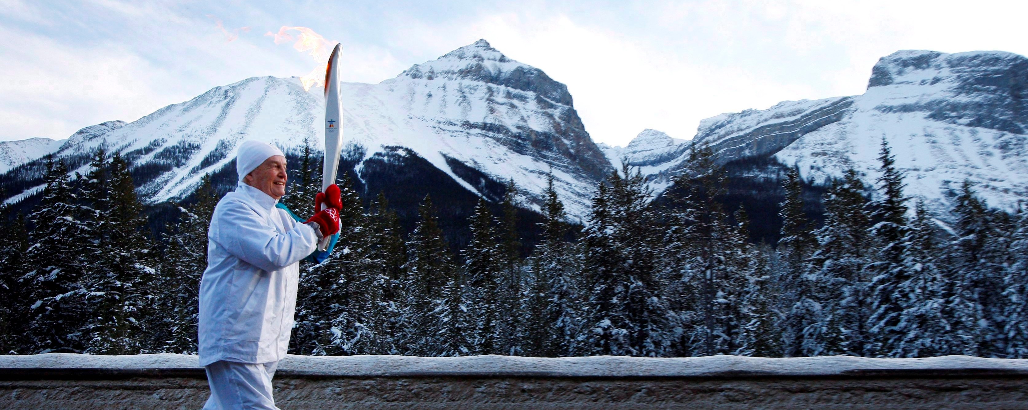 Peter Lougheed dressed warmly running with the olympic torch through the Rocky Mountains