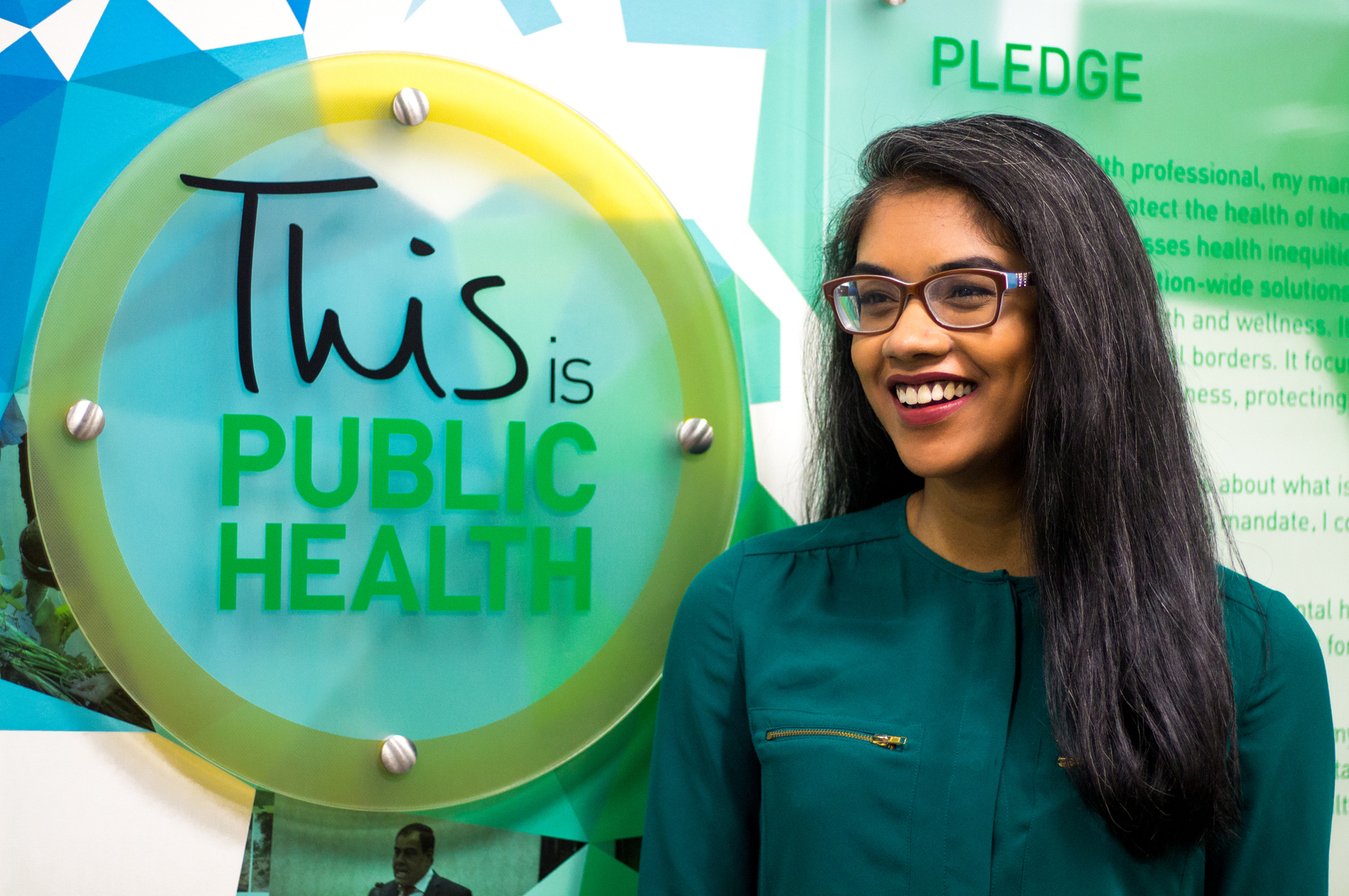 Tharsini posing in front of the This is Public Health display